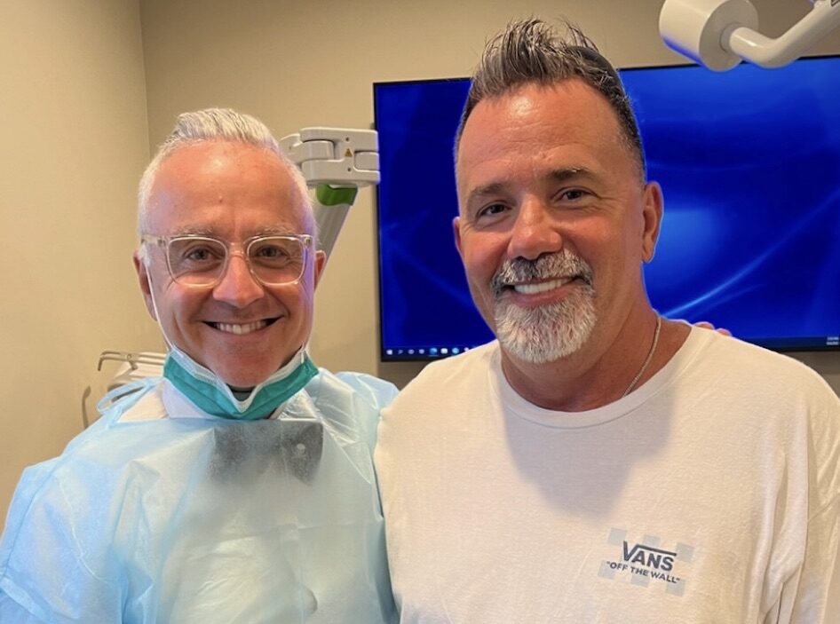 Dr. Joe Mehranfar in surgical attire beside a smiling dental implant patient